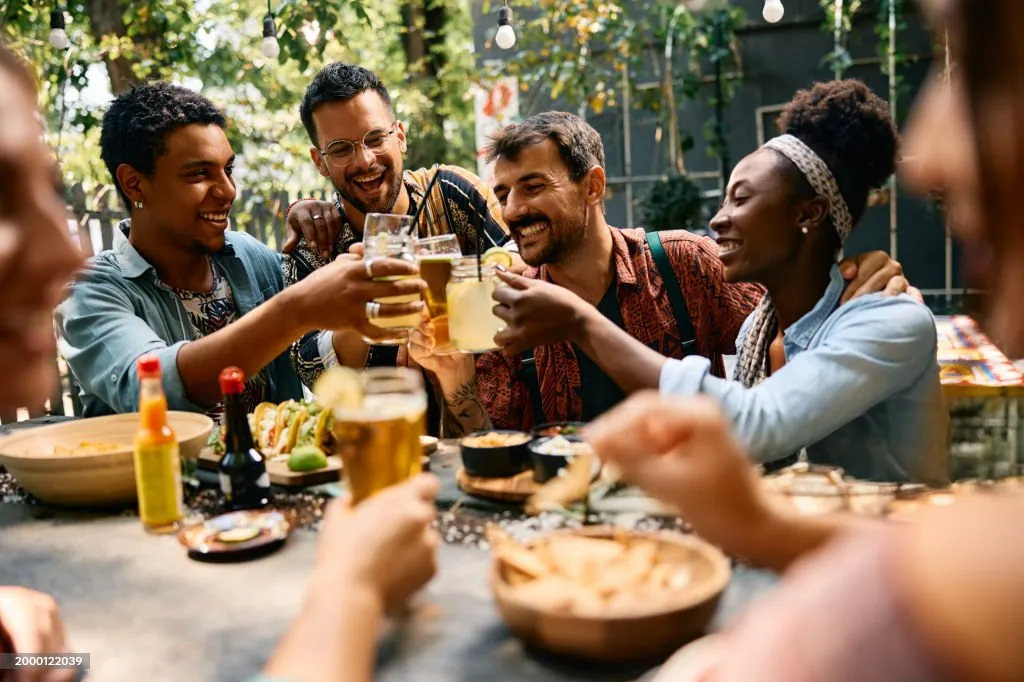 Friends laughing and toasting at an outdoor restaurant table