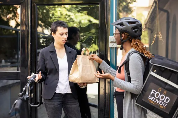A courier handing a takeaway order to a customer at the door